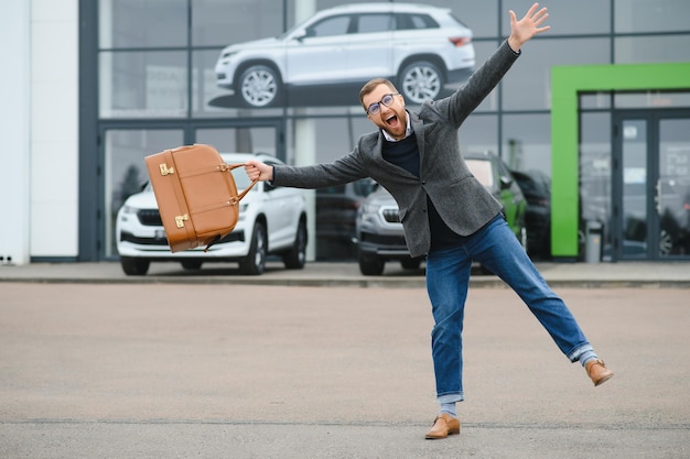 Happy buyer near the car in front of the modern avtosalon building