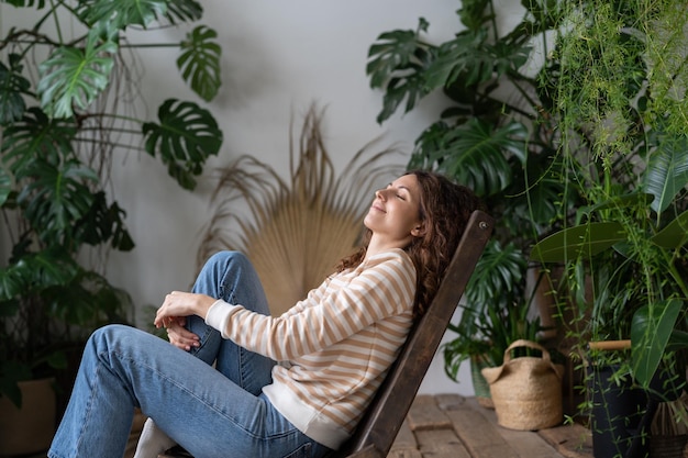 Happy calm peaceful woman dreaming with closed eyes and smile on face in tropical greenhouse