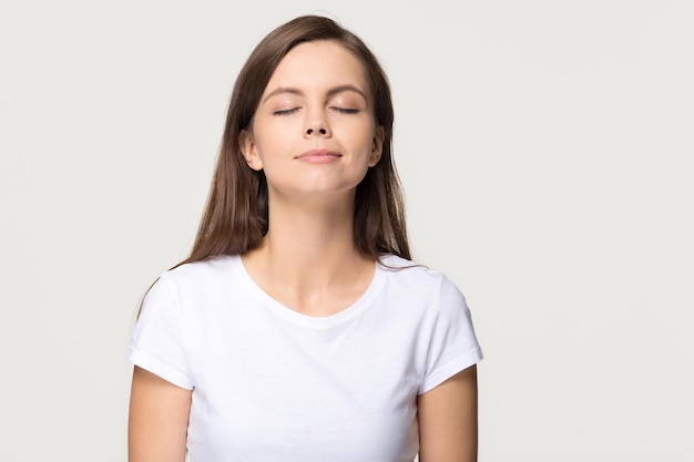 Happy calm teen girl enjoying good smell or pleasant fragrance serene mindful young woman taking deep breath feel no stress free inhaling fresh air relaxing isolated on white grey studio background