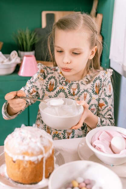 幸せな率直な小さな子供8歳の女の子は自宅のキッチンで楽しい準備ができている春のイースター休暇を持っています