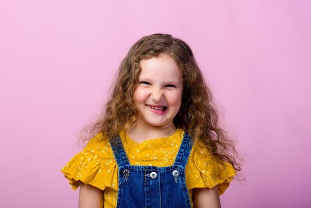 Emozioni felici del bambino spensierato. energica gioiosa adorabile bambina che ride di scherzo su sfondo rosa in studio.