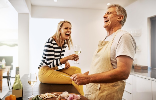 Happy and carefree couple cooking dinner laughing and enjoying the weekend in the kitchen at home A mature husband relaxing and preparing a meal or lunch for his wife while having fun