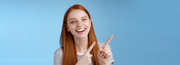 Happy carefree smiling redhead caucasian girl ginger straight hairstyle pointing upper left corner