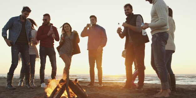해가 지기 시작할 때 해변에서 모닥불 옆에서 맥주를 마시며 즐거운 시간을 보내는 평온한 젊은 친구들