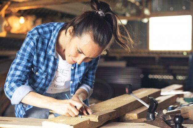 幸せな大工女が家のワークショップで木の板測定テープを測定します。