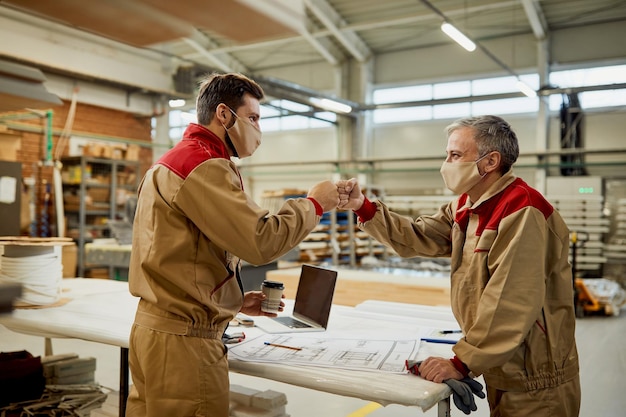 Happy carpenters fist bumping while working in a workshop during coronavirus pandemic