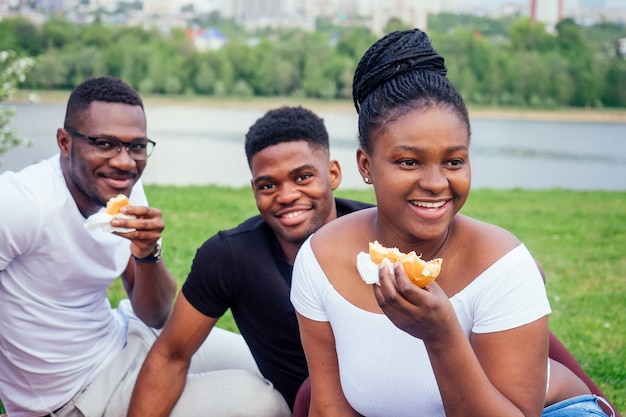 Happy casual america african people having fun and eating burger outdoors lifestyle,students for a break summer evening cloudy weather in park