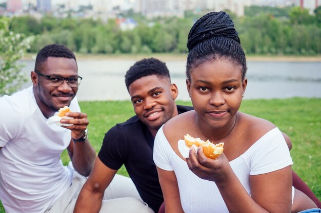 Happy casual america african people having fun and eating\
burger outdoors lifestylestudents for a break summer evening cloudy\
weather in park