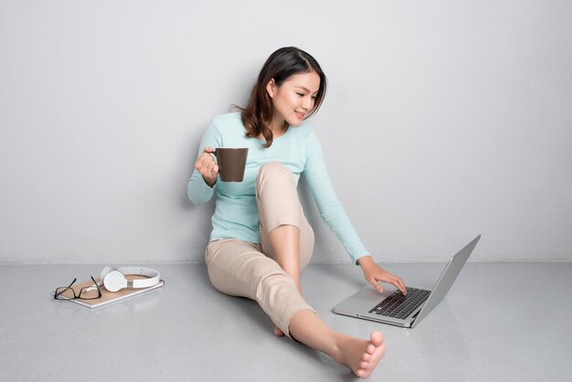 Happy casual beautiful asian woman working on a laptop sitting on floor at home