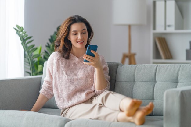 Felice casual bella donna sta usando un telefono seduto su un divano a casa