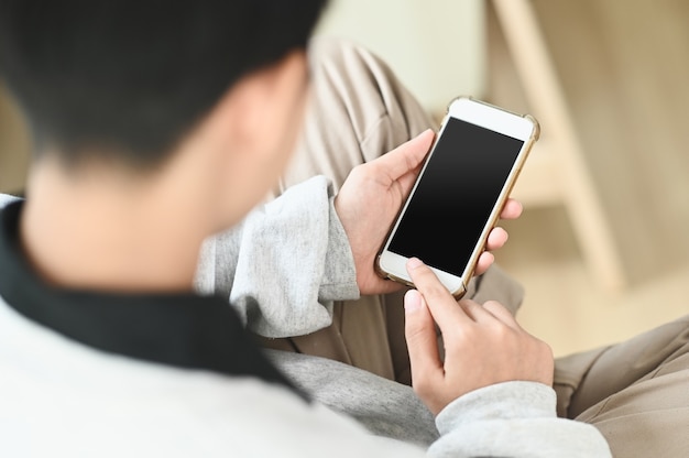 La bella donna casuale felice sta usando smartphone con lo schermo bianco e si siede su un divano a casa