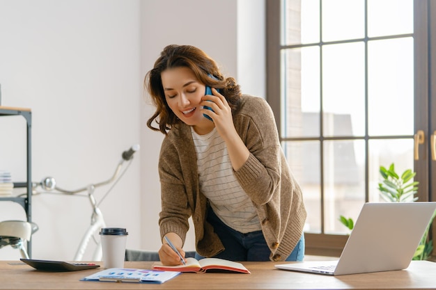 Photo happy casual beautiful woman working on a laptop and talking by phone in the office