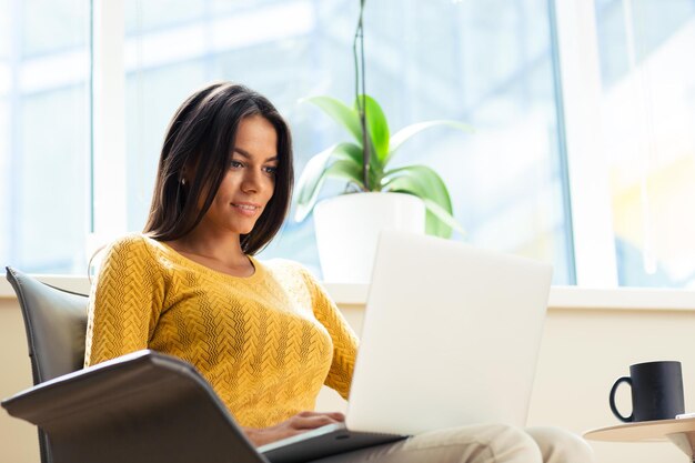 Happy casual businesswoman sitting on office chair with laptop in office