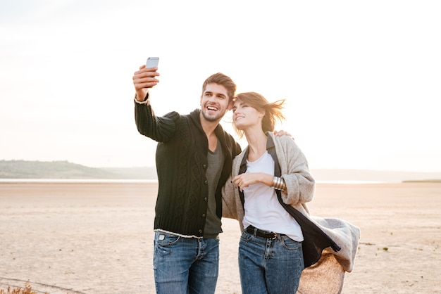 햇빛 아래 해변에 함께 서서 셀카 사진을 찍는 행복한 캐주얼 커플