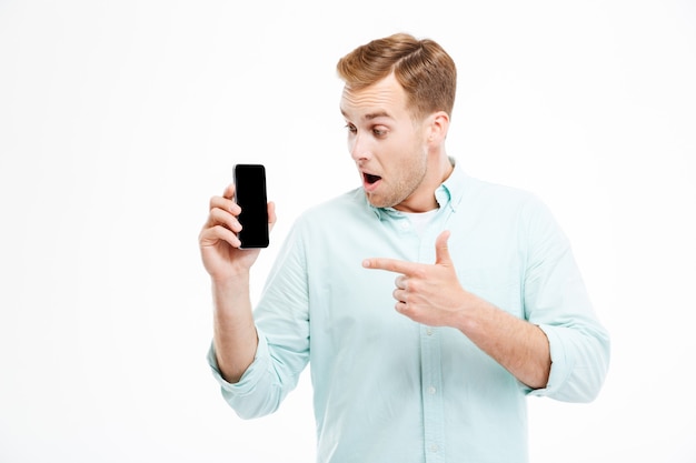 Felice uomo casual che punta il dito sullo schermo dello smartphone sul muro bianco