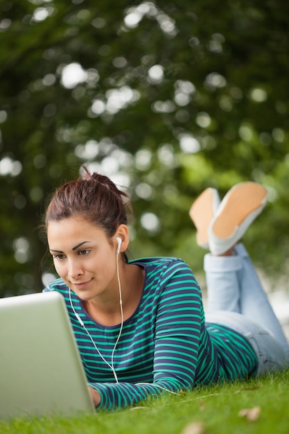 Happy casual student lying on grass using laptop