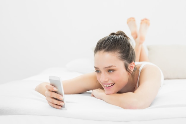 Happy casual woman looking at mobile phone in bed