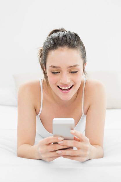 Happy casual woman looking at mobile phone in bed