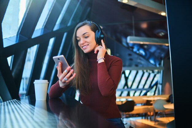 Happy casual woman with black wireless headphones holds mobile phone and enjoys music. Modern people with audio mobility lifestyle