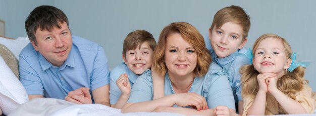 Happy caucasian big family lie in bedroom on bed and smile dressed in blue