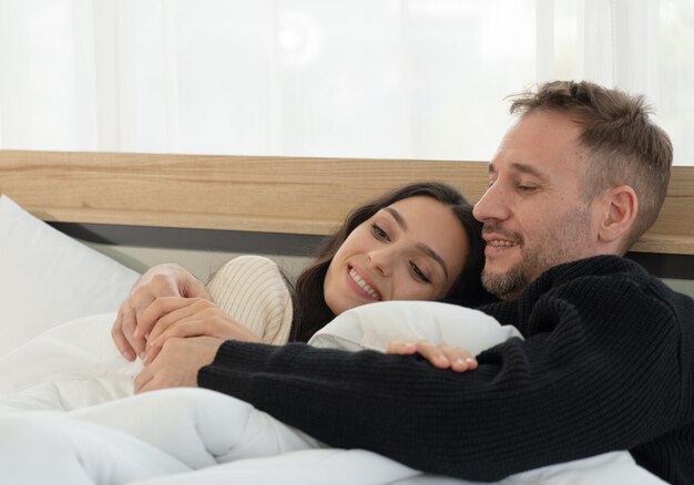 Photo happy caucasian couple lying in the bed in bedroom at home in the morning