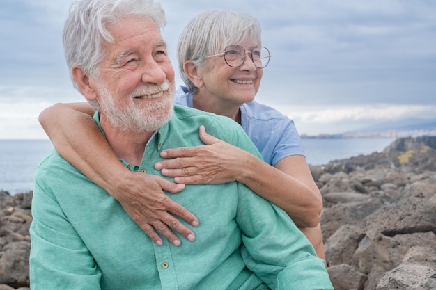 Happy caucasian elderly couple hugging sitting in outdoors at sea Two senior people enjoying freedom and relax in retirement Horizon over water