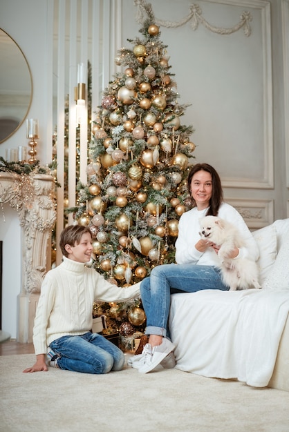 Happy caucasian family mother and son sitting at home near christmas tree with their little dog fami...