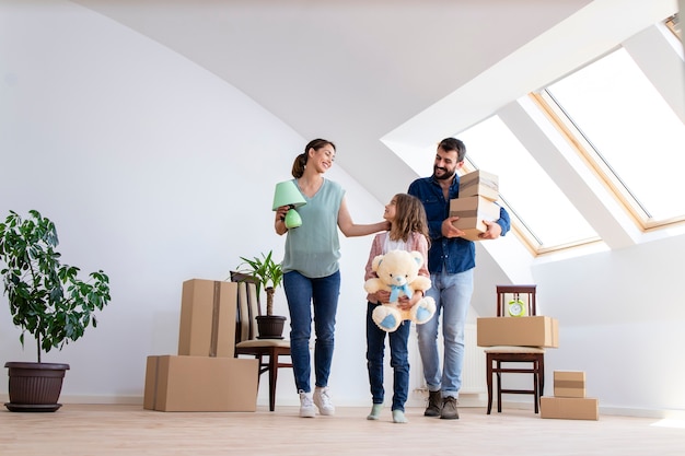 Happy caucasian family moving in new apartment with cute little girl carrying boxes and belongings.