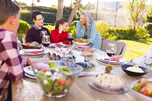 Happy caucasian family sitting at table and eating dinner together in sunny garden. Spending family time at home.