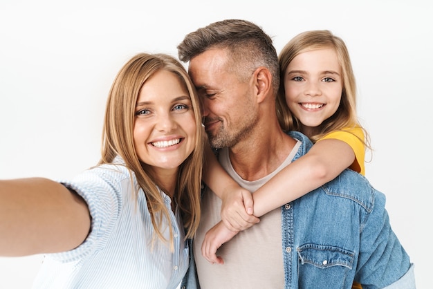 Happy caucasian family woman and man with little girl smiling and taking selfie photo together isolated on white