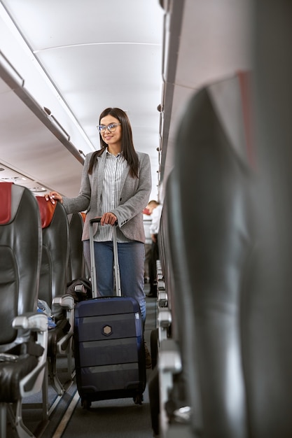 Happy caucasian female passenger with luggage in airplane salon