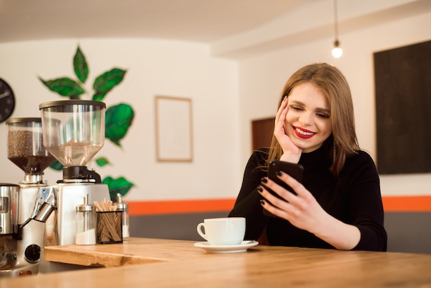 Happy Caucasian female watching her photo on cell telephone while relaxing in cafe.