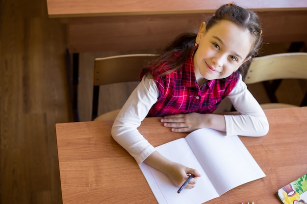 Happy caucasian girl sitting at desk in class room and begins to draw in a pure notebook. 