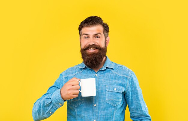 Happy caucasian guy holding tea mug yellow background