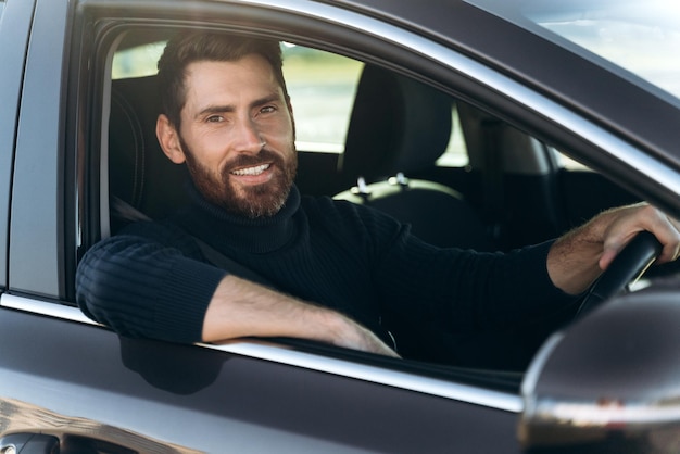 행복한 백인 남자가 차 옆으로 긴 길을 가는 동안 앉아서 창을 바라보고 있습니다. 바쁜 사람들과 교통 개념