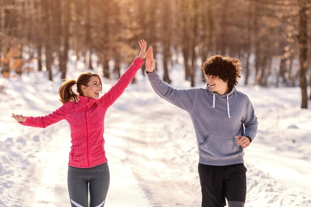 Happy Caucasian runners giving high five during running on the cold weather. Snow all around, wintertime.