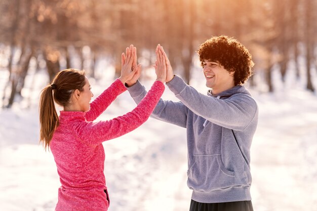 Happy Caucasian runners giving high five during running on the cold weather. Snow all around, wintertime.