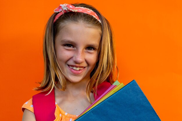 Happy caucasian schoolgirl with school bag and books over orange background at elementary school