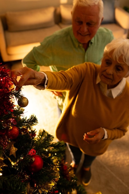 Foto una felice coppia di anziani caucasici che decorano l'albero di natale nel soggiorno a casa