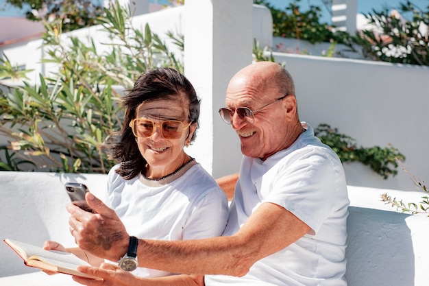 Happy caucasian senior couple relaxing sitting in a bench woman with a book and man with phone