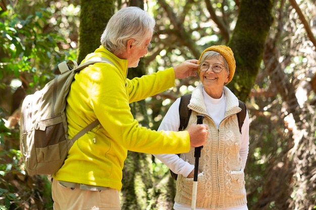 Happy caucasian senior couple with backpack and walking sticks\
hike in the forest enjoying healthy lifestyle and retirement