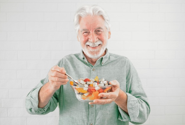 Happy caucasian senior man holding a glass bowl with fresh summer fruit salad ready to eat