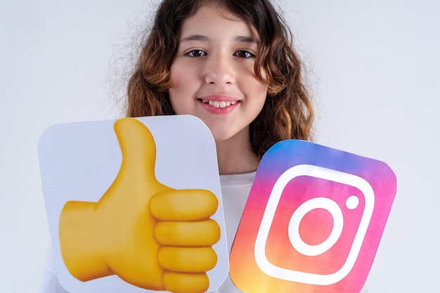 Happy caucasian teen girl in black tshirt holding instagram
logo and thumbs up emoji sign