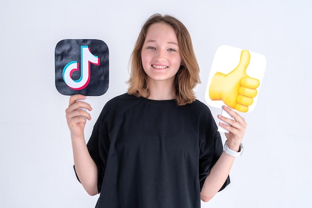 Tiktok 로고와 이모티콘 기호를 들고 검은 티셔츠에 행복 백인 십 대 소녀