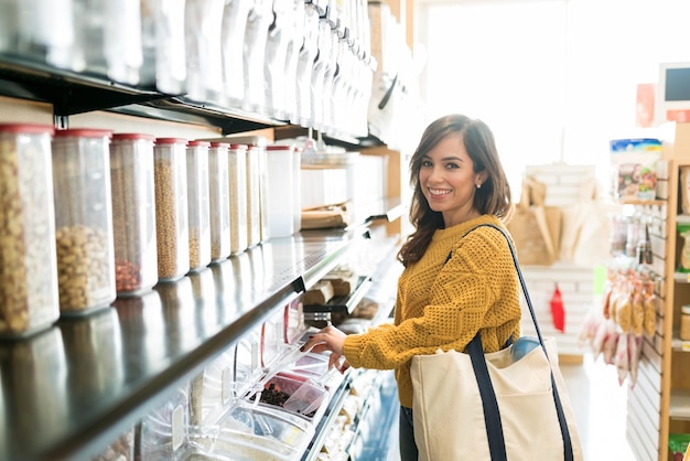 Happy Caucasian woman carrying bag while buying food in bulk in supermarket