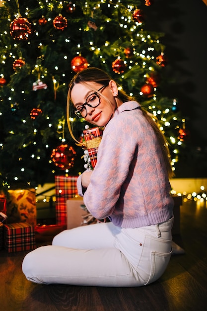 Happy caucasian woman holding big Christmas present near Christmas tree.