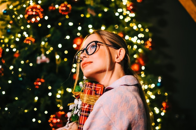 Foto donna caucasica felice che tiene grande regalo di natale vicino all'albero di natale.