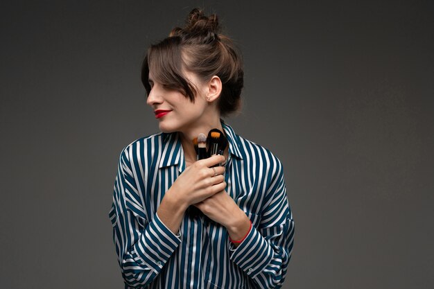 Happy caucasian woman holds makeup brushes isolated on grey background