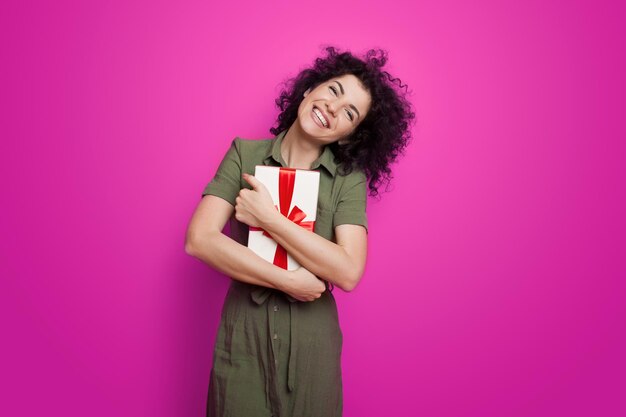 Happy caucasian woman hugging gift box isolated over pink background girl in love receiving gift cur...