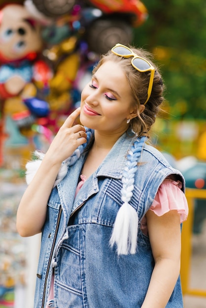 Happy Caucasian woman with blue pigtails in a denim vest in an amusement park enjoying the weekend